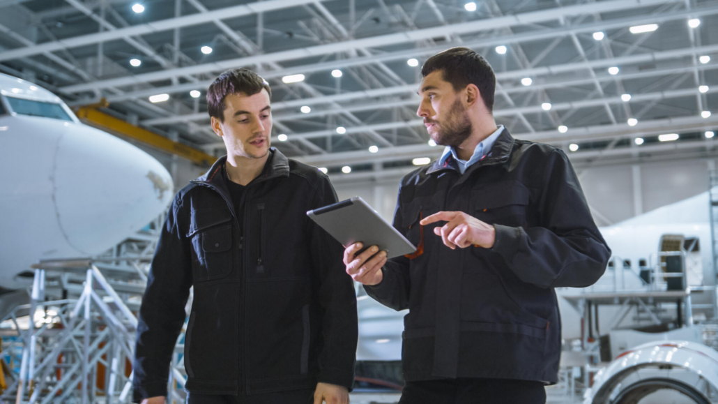 Team of Aircraft Maintenance Mechanics Moving through Hangar. Holding Tablet Computer